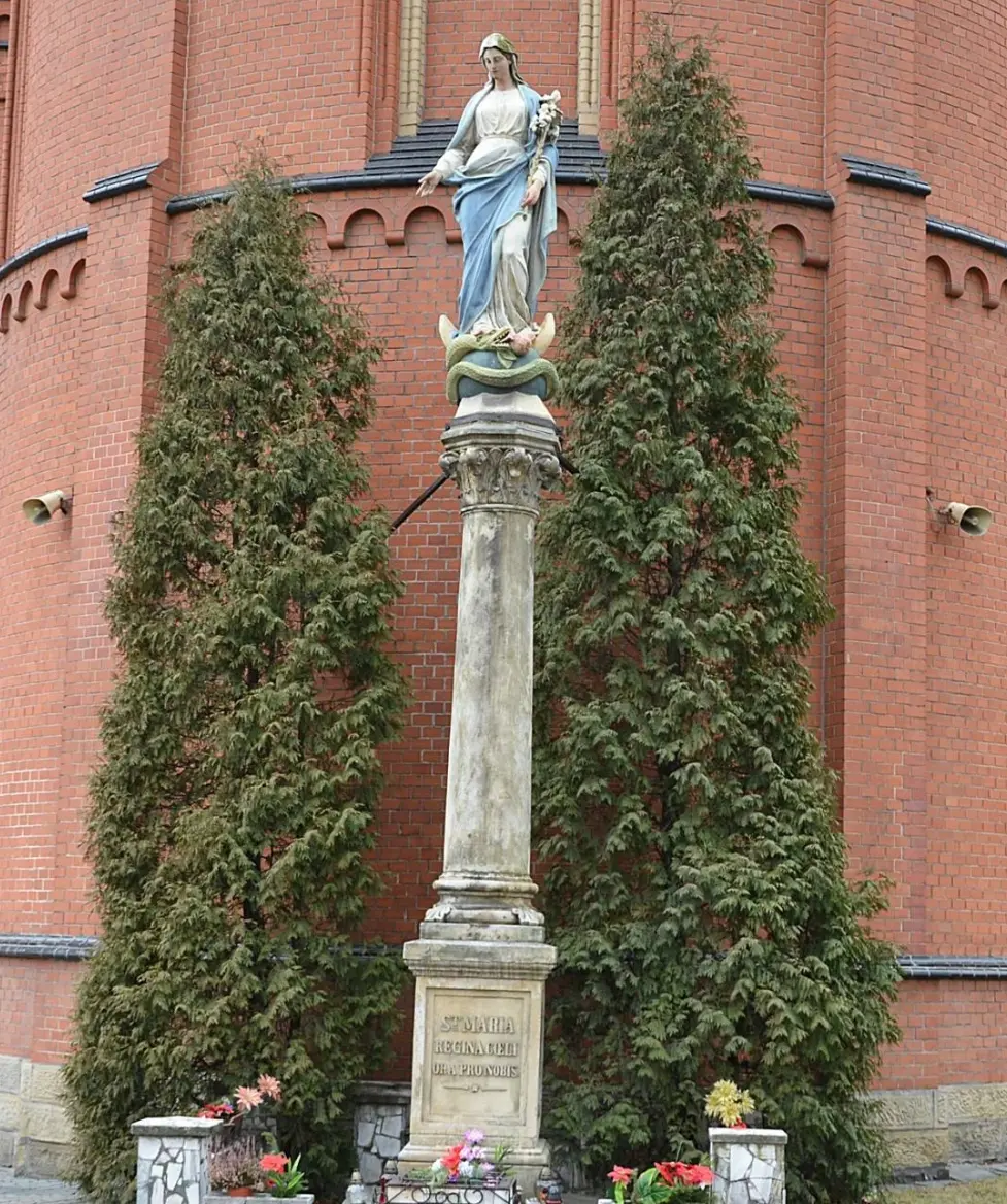 Średni kadr na figurę Matki Boskiej w otoczeniu zieleni na tle ceglanej fasady kościoła